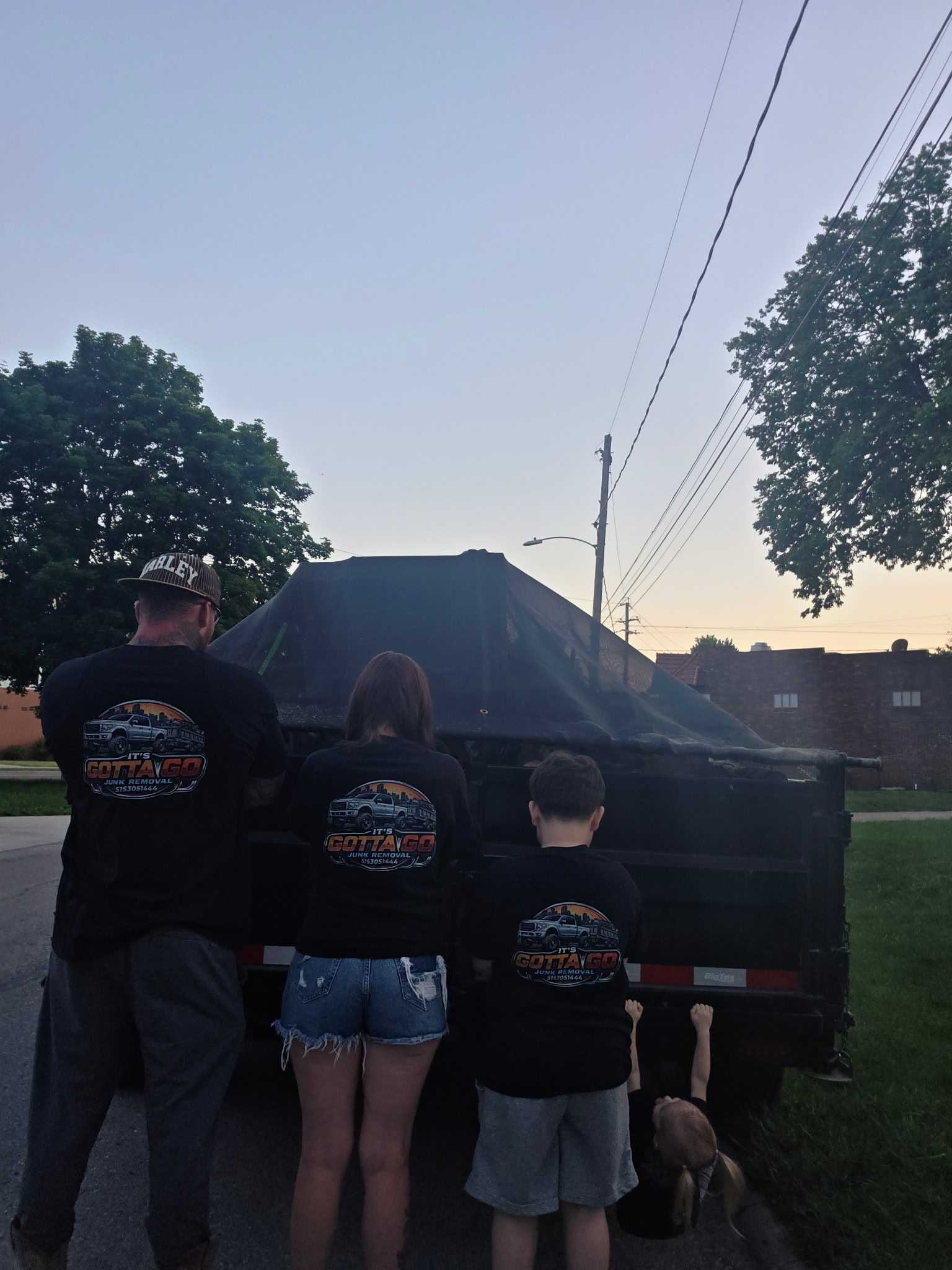 Its Gotta Go crew in branded shirts standing in front of loaded trailer at dusk
